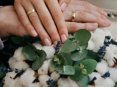 Mains des mariés portant leurs alliances, posées sur un bouquet