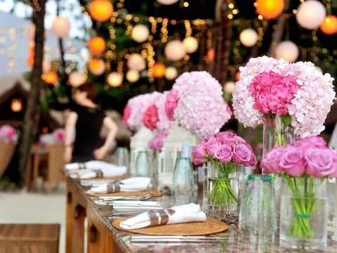 Table dressée avec bouquets de fleurs roses sous des guirlandes lumineuses