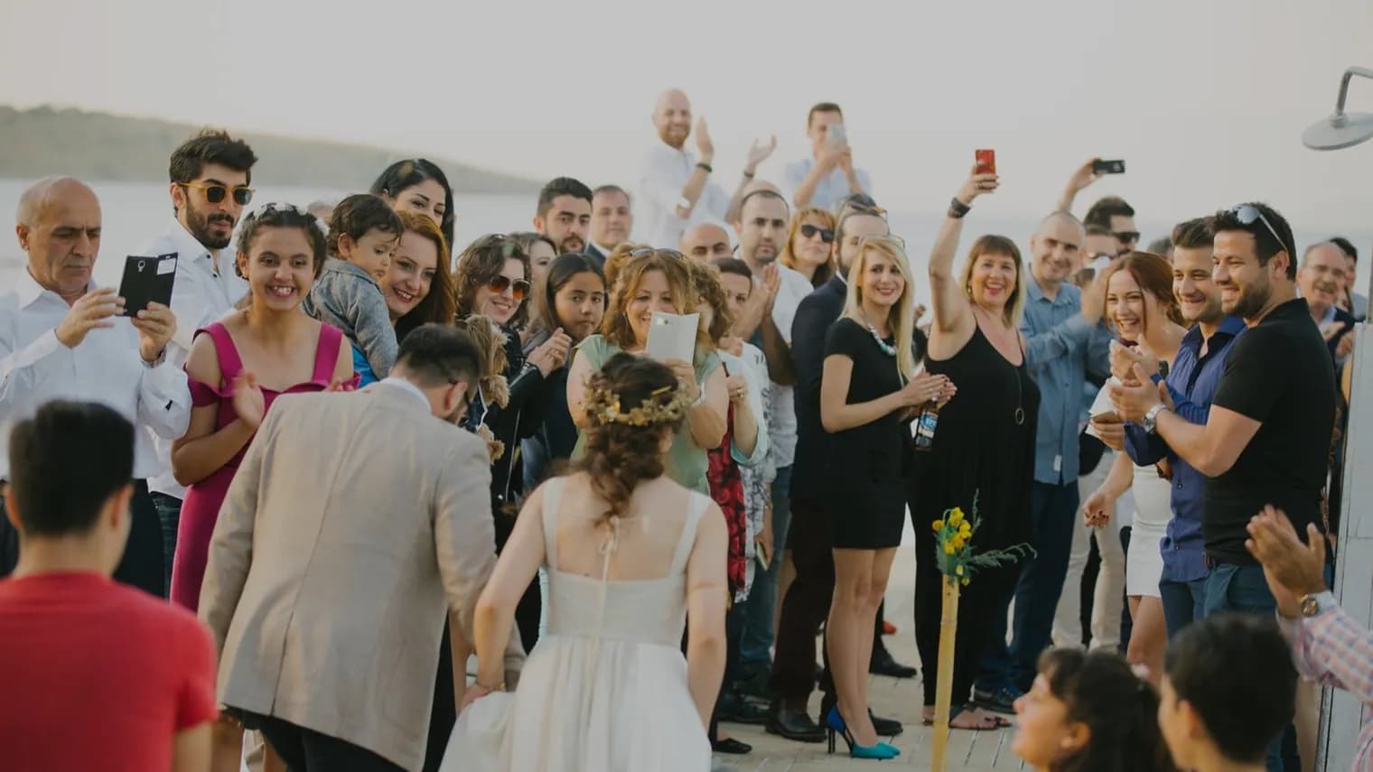 Une foule d'invités entoure la mariée, plusieurs d'entre eux la photographient avec leur téléphone